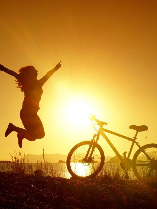 Woman jumping next to her bike at sunset after cycling in Andalucia. 20 Best Routes for Cycling in Andalucia in 2023