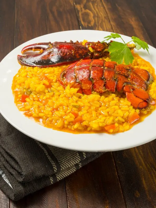 arroz con bogavante, rice with lobster in a white plate on a wooden table.