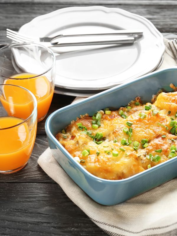 chorizo casserole in a pan next to 2 glasses of orange juice and a plate. Simple Spanish Chorizo Casserole Recipe