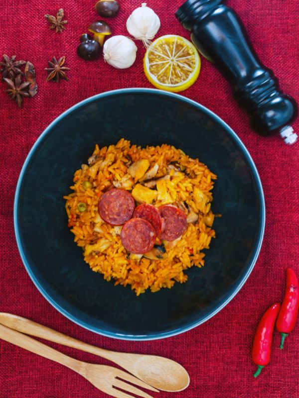 chorizo paella in a black bowl on a red table cloth. Rich Chorizo Paella Recipe from Spain