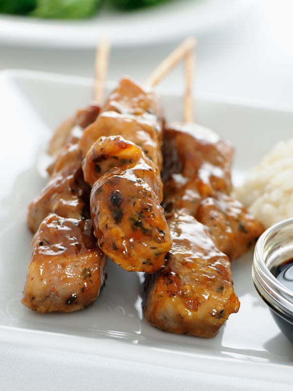 closeup with Spanish pork skewers recipe on a white plate with sauce and rice