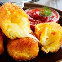 closeup with Spanish potato croquettes recipe filled with cheese and served with red sauce.