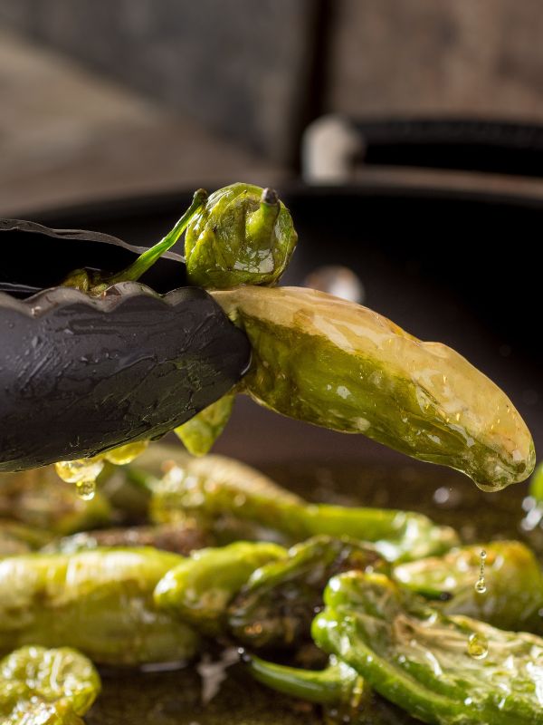 closeup with padron peppers being fried in a pan