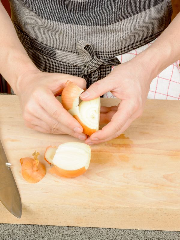 cook peeling an onion on a wooden board for the vegan spanish  omelette.