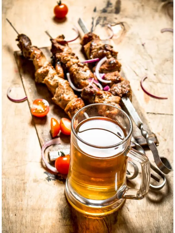 pork skewers on a serving plate next to a pint of beer.