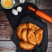 shrimp empanadas on a black towel on a wooden table with an egg next to them.