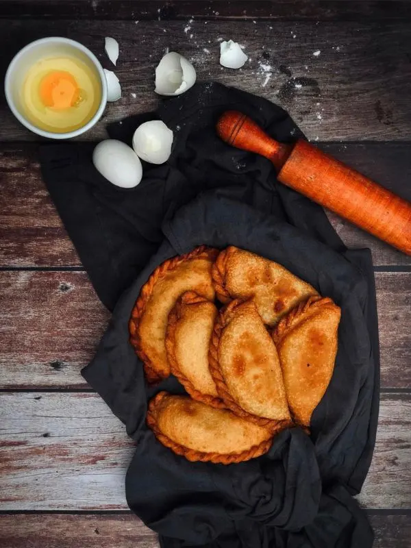 shrimp empanadas on a black towel on a wooden table with an egg next to them.