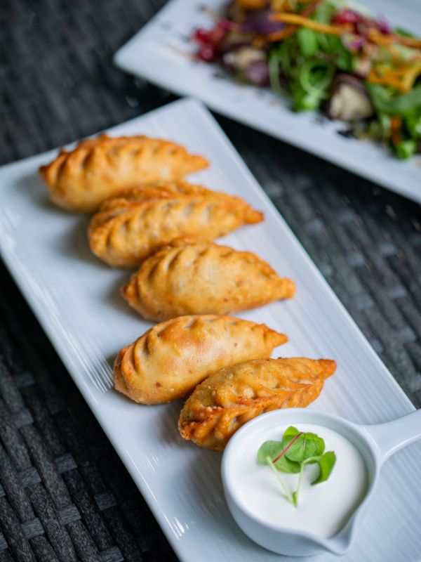 cheese empanada recipe on a white plate next to sauce and salad.