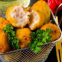 spanish potato croquettes with ham in a serving basket, on a black plate, next to red peppers and a drink, top 10 tapas dishes