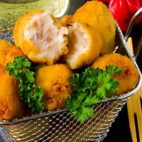 spanish potato croquettes with ham in a serving basket, on a black plate, next to red peppers and a drink, top 10 tapas dishes