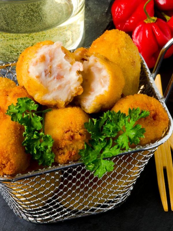 spanish potato croquettes with ham in a serving basket, on a black plate, next to red peppers and a drink