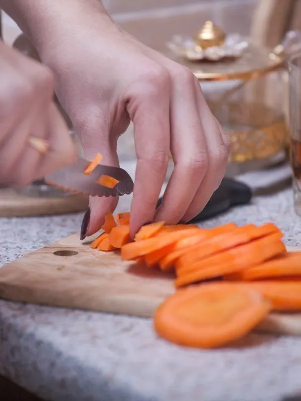 woman cutting a carrot on a cutting board for the marinated carrots recipe