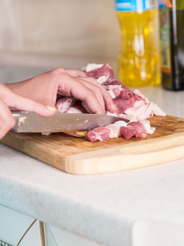 woman cutting the meat on a wooden board for the pork skewers recipe.