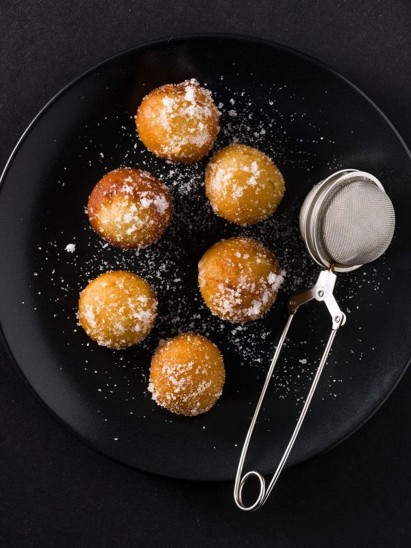 fried fritters on a black plate, dusted with powdered sugar