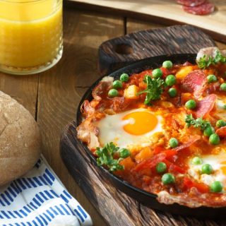 Huevos a la flamenca in a pan next to a glass of orange juice, food of Andalucia