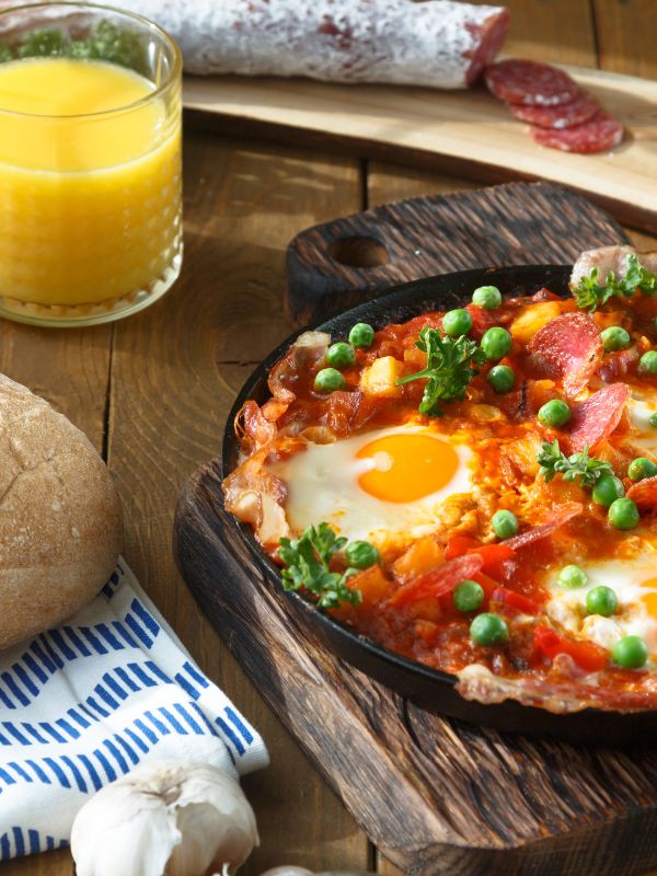 Huevos a la flamenca in a pan next to a glass of orange juice - Best Huevos a la Flamenca Recipe
