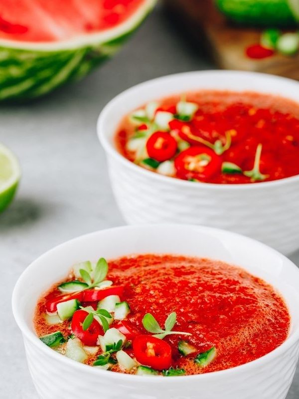 carrot Gazpacho in 2 bowls with a watermelon in the background.