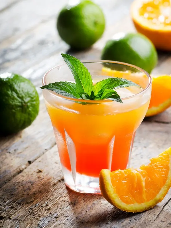 agua de valencia in a small glass with oranges and limes next to it.