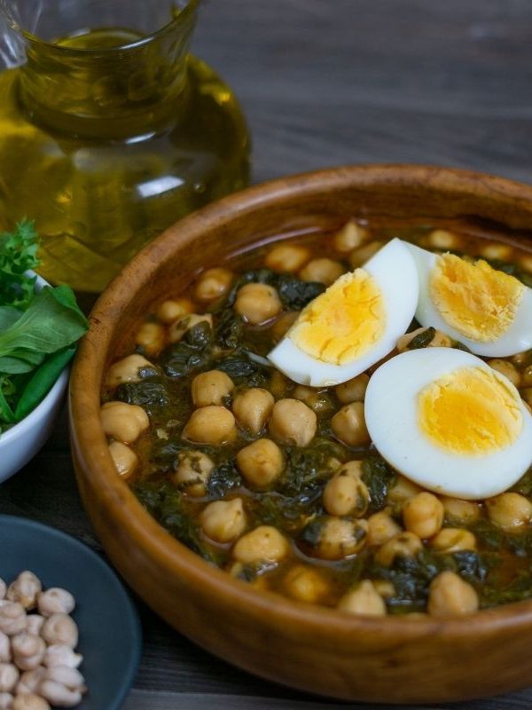 chickpea and spinach stew, potaja de vigilia, in a clay bowl served with boiled egg.