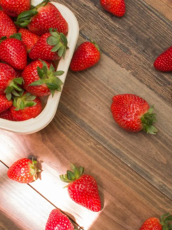 fresh strawberries in a bowl and on a wooden table.