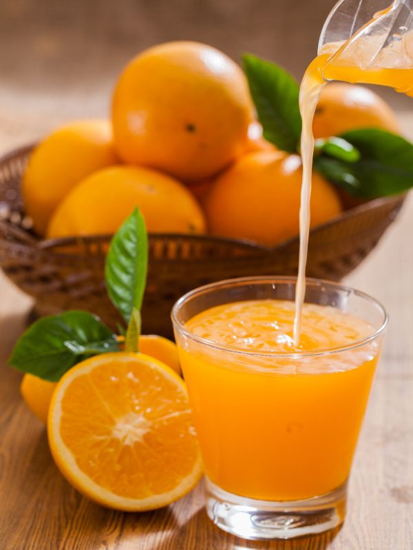 freshly squeezed orange juice being poured on a glass with oranges in the basket at the back