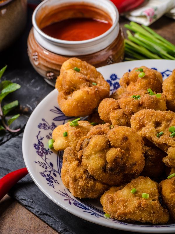 fried cauliflower recipe in a bowl next to some red sauce. 20 Best Spanish Vegetarian Tapas You Will Love