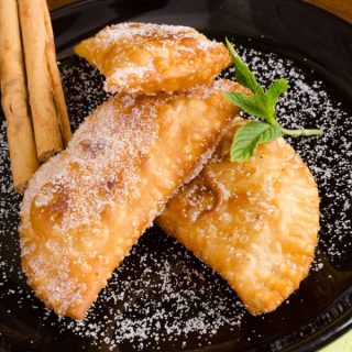 fruit empanada recipe on a black plate dusted with sugar