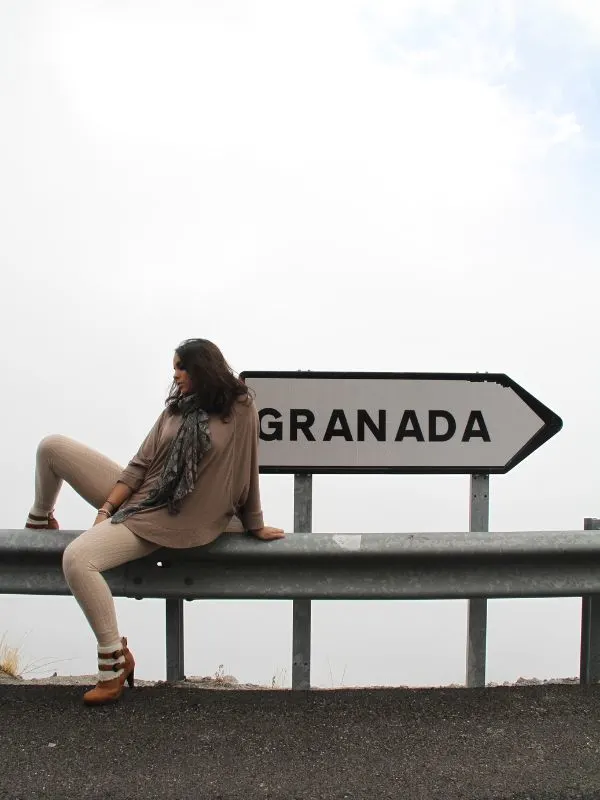 girl sitting next to a road sign with granada