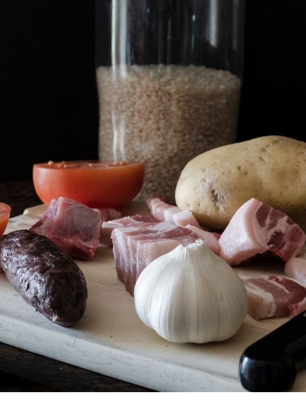 ingredients for spanish baked rice like rice, black pudding, bacon, potatoes and tomatoes