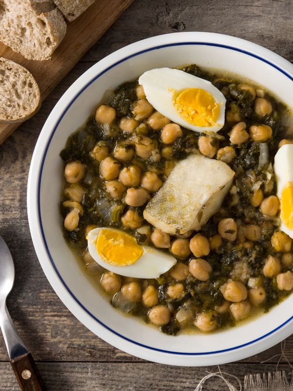 potaje de vigilia with chickpeas, spinach and cod served in a white bowl with bread