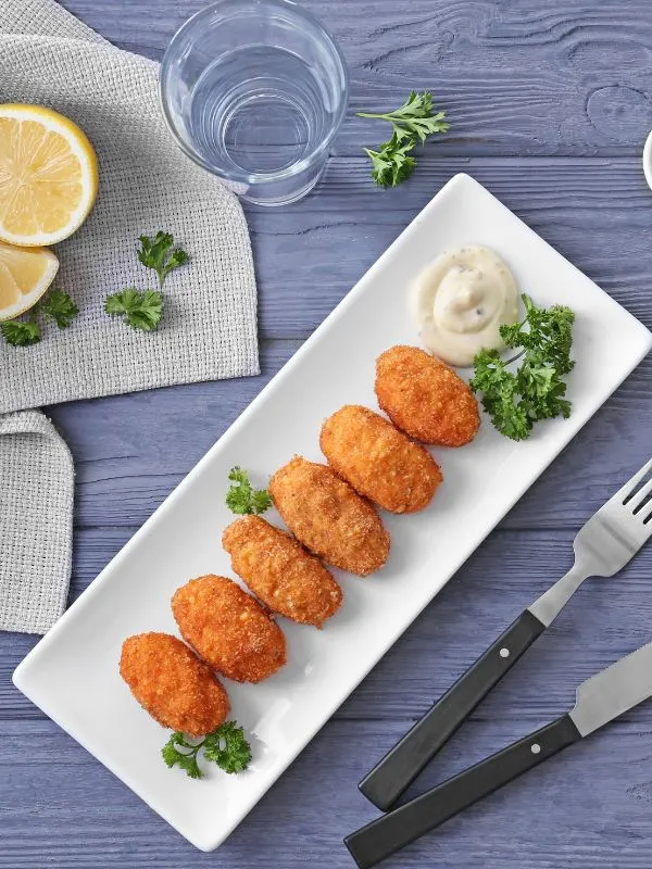 shrimp croquettes on a white plate next to a glass of water and lemon slices.