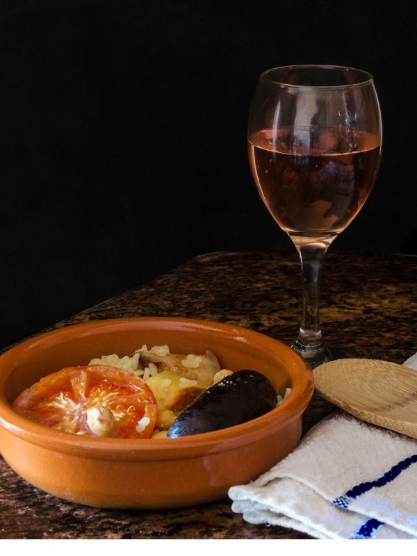 spanish baked rice in a clay pot next to a glass of wine.