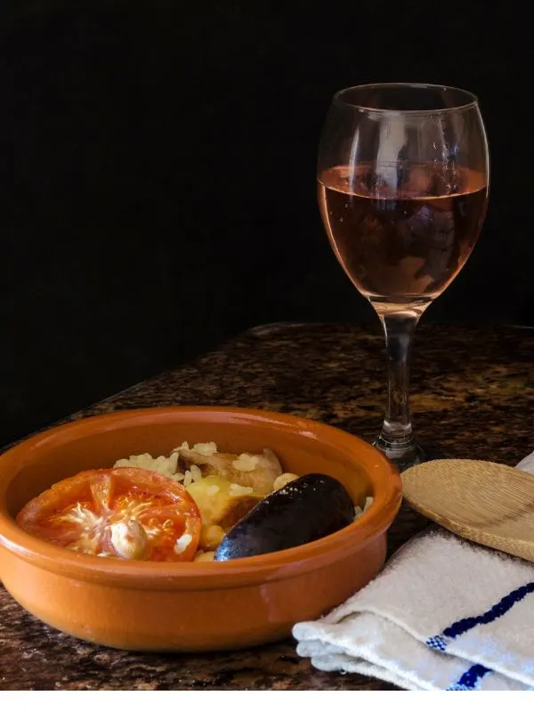 spanish baked rice in a clay pot next to a glass of wine.