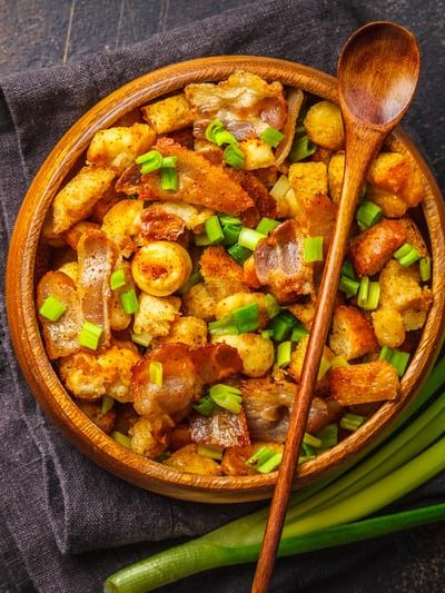 Spanish migas with pork and green onions in wooden bowl on a dark background.