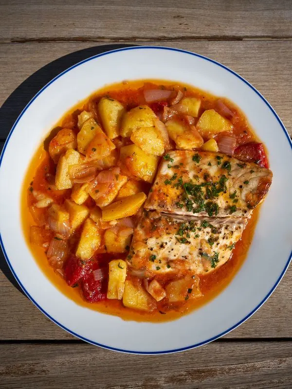 spanish sea bass served with potatoes in a white plate.