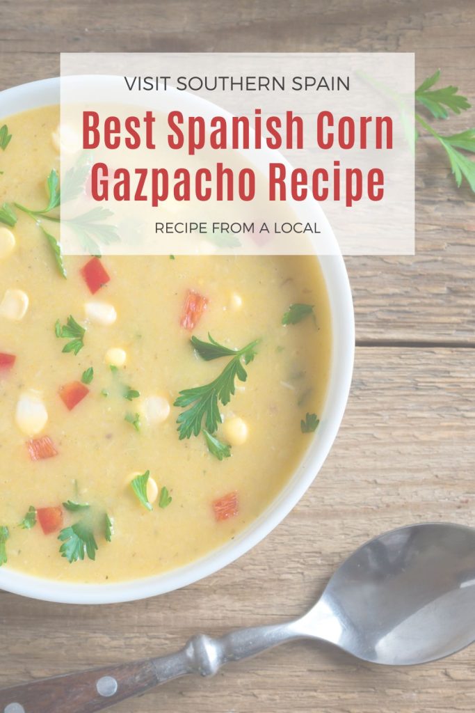 closeup with corn soup decorated with corn, peppers and parsley. On top it's written best spanish corn gazpacho recipe. 