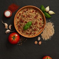 a bowl of Quinoa Spanish Rice with ingredients next to it on a black surface.