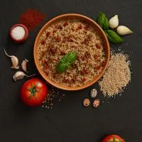 a bowl of Quinoa Spanish Rice with ingredients next to it on a black surface.