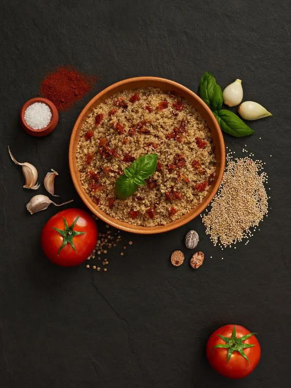 a bowl of Quinoa Spanish Rice with ingredients next to it on a black surface. Healthy Quinoa Spanish Rice Recipe