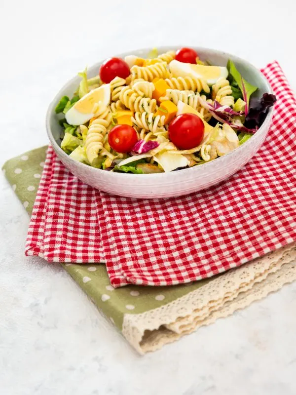 a bowl of spanish macaroni pasta with egg, tomatoes and veggies on kitchen tablecloths. Light Spanish Macaroni Salad Recipe