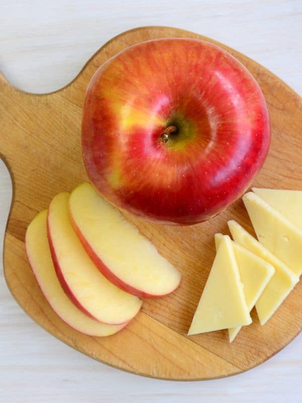 an apple, slices of manchego on a wooden board for the apple manchego salad