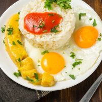 arroz a la cubana, rice with eggs and bananas on a white plate