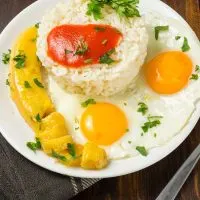 arroz a la cubana, rice with eggs and bananas on a white plate