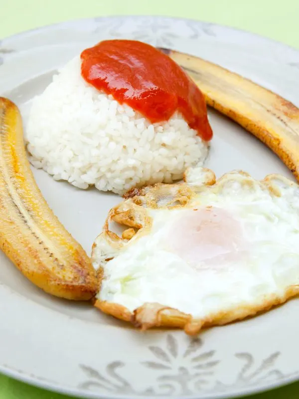 arroz a la cubana, rice with tomato sauce, bananas and egg on a plate.