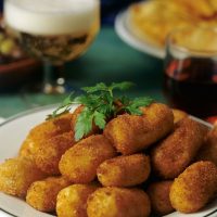 bacalao croquettes on a white plate with a glass of beer in the background
