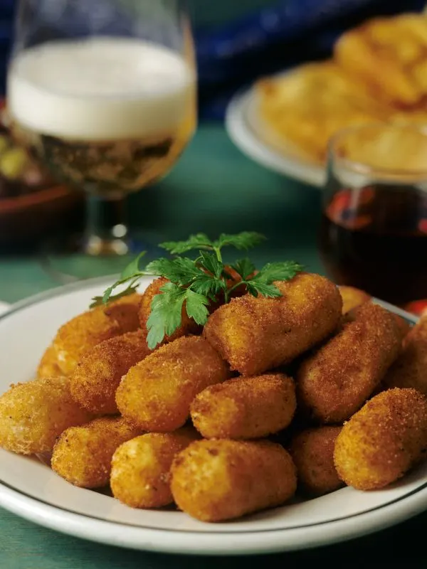 bacalao croquettes on a white plate with a glass of beer in the background