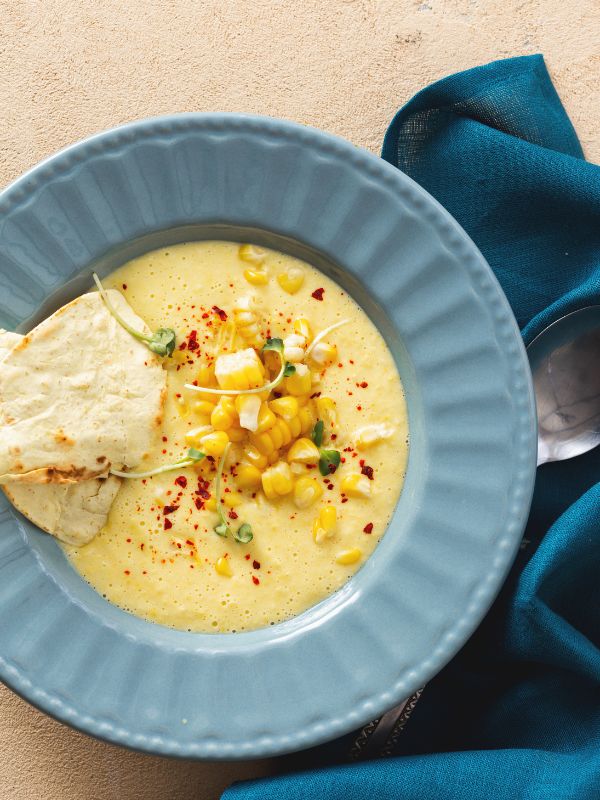 sweet corn gazpacho in a blue bowl served with flat bread.