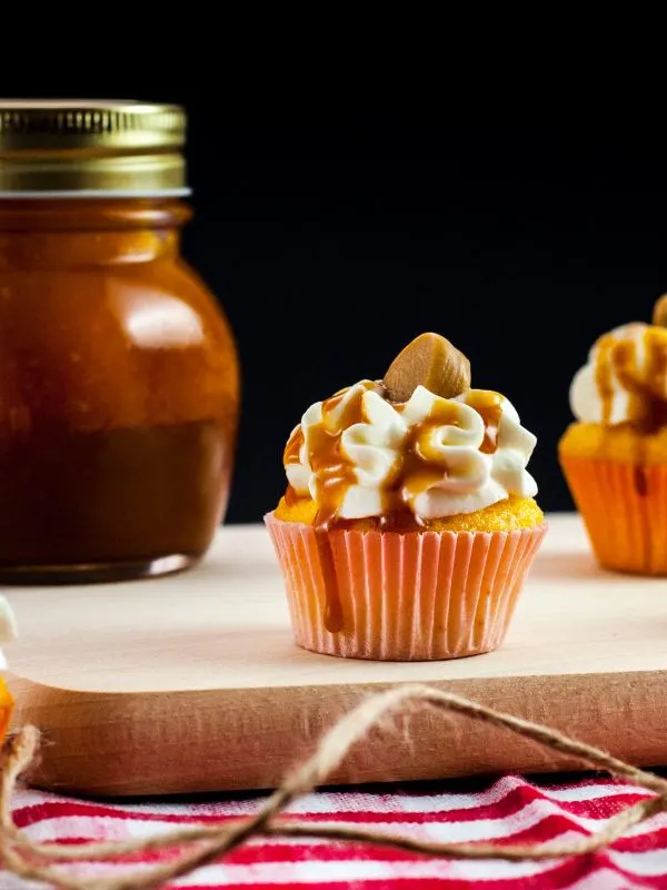 dulce de leche cupcakes on a wooden board with a jar of dulce de leche in the background.