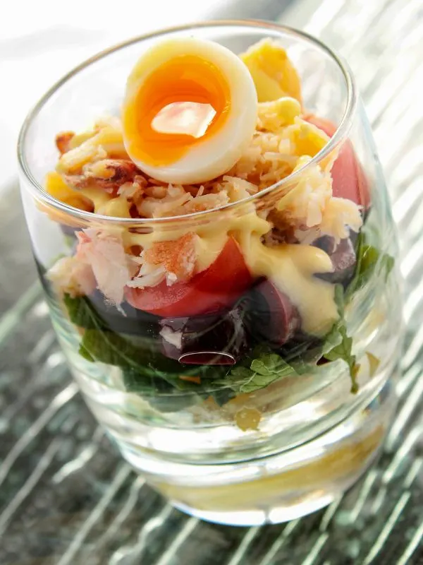 ensalada de cangrejo, crab salad served in a glass with a boiled egg on top.