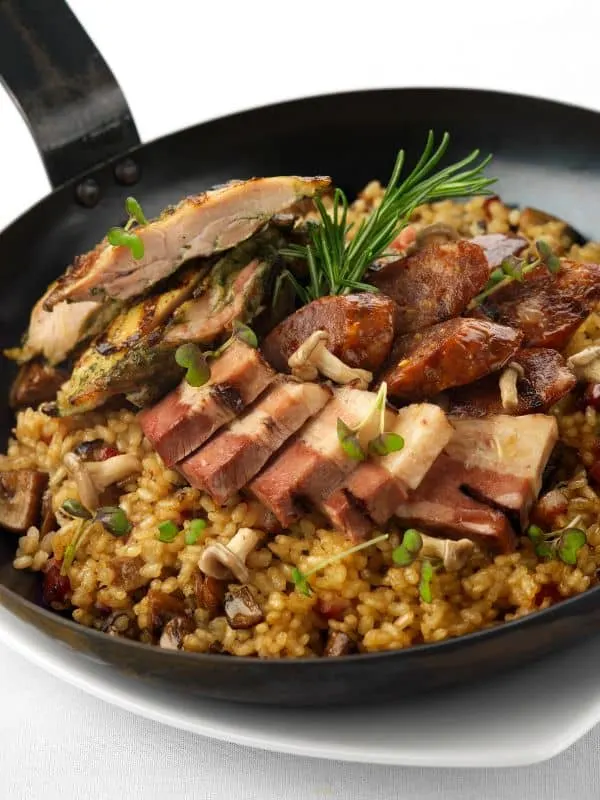 meat Paella served in a pan with bacon sausage and meat - Rich Spanish Meat Paella Recipe